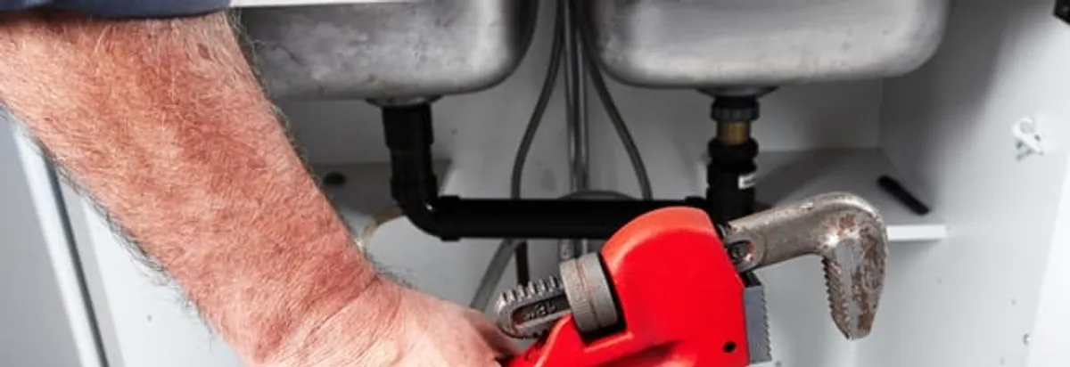 Garbage disposal repair technician tightening drain connections under a kitchen sink in Fargo, ND
