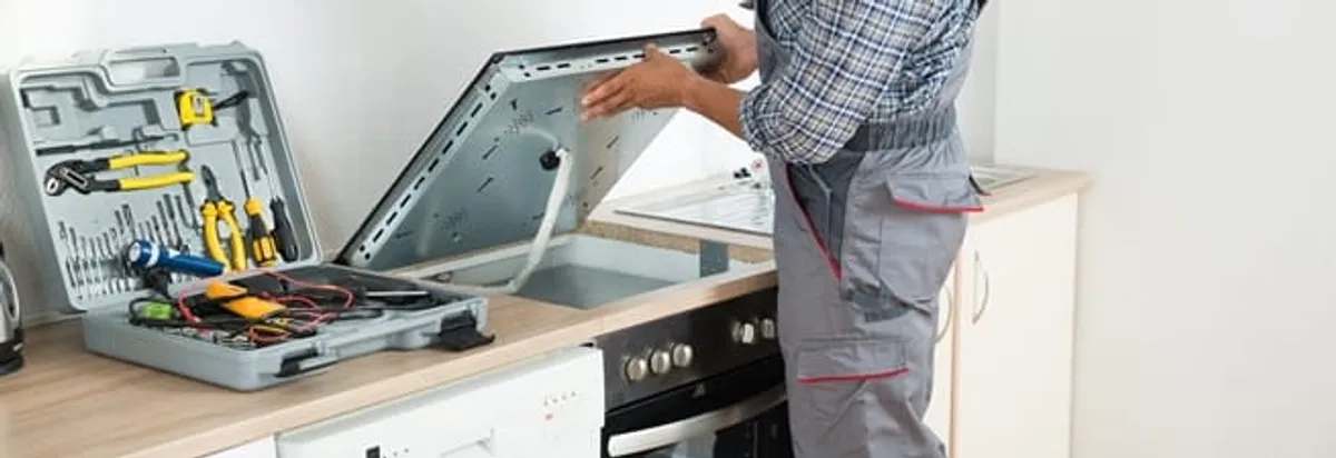 Cooktop repair technician lifting a built-in stovetop for service in Fargo, ND