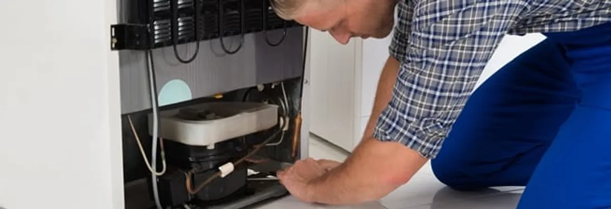 Refrigerator repair technician servicing the compressor and condenser area in Fargo, ND