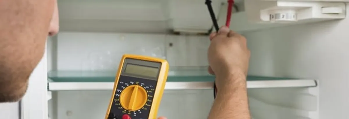Refrigerator repair technician testing electrical components with a multimeter in Fargo, ND